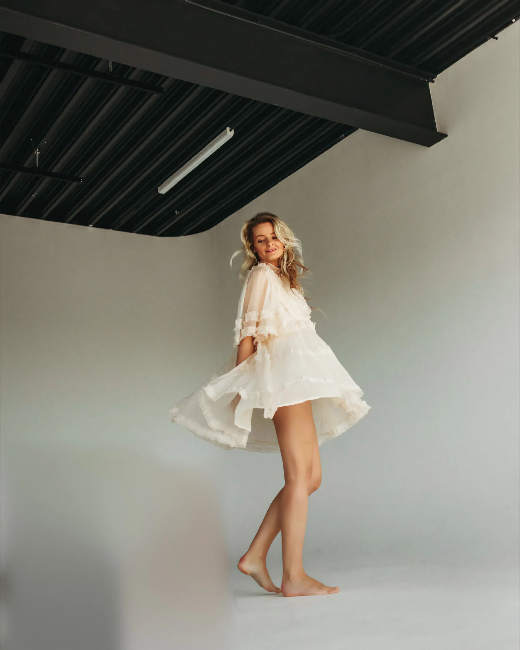 Veronika mid‑twirl in a sheer cream dress, hair caught in the studio fan